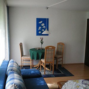 Wohn- Esszimmerkombination mit blauem Polstermöbel, kleiner Tisch mit drei Stühlen  